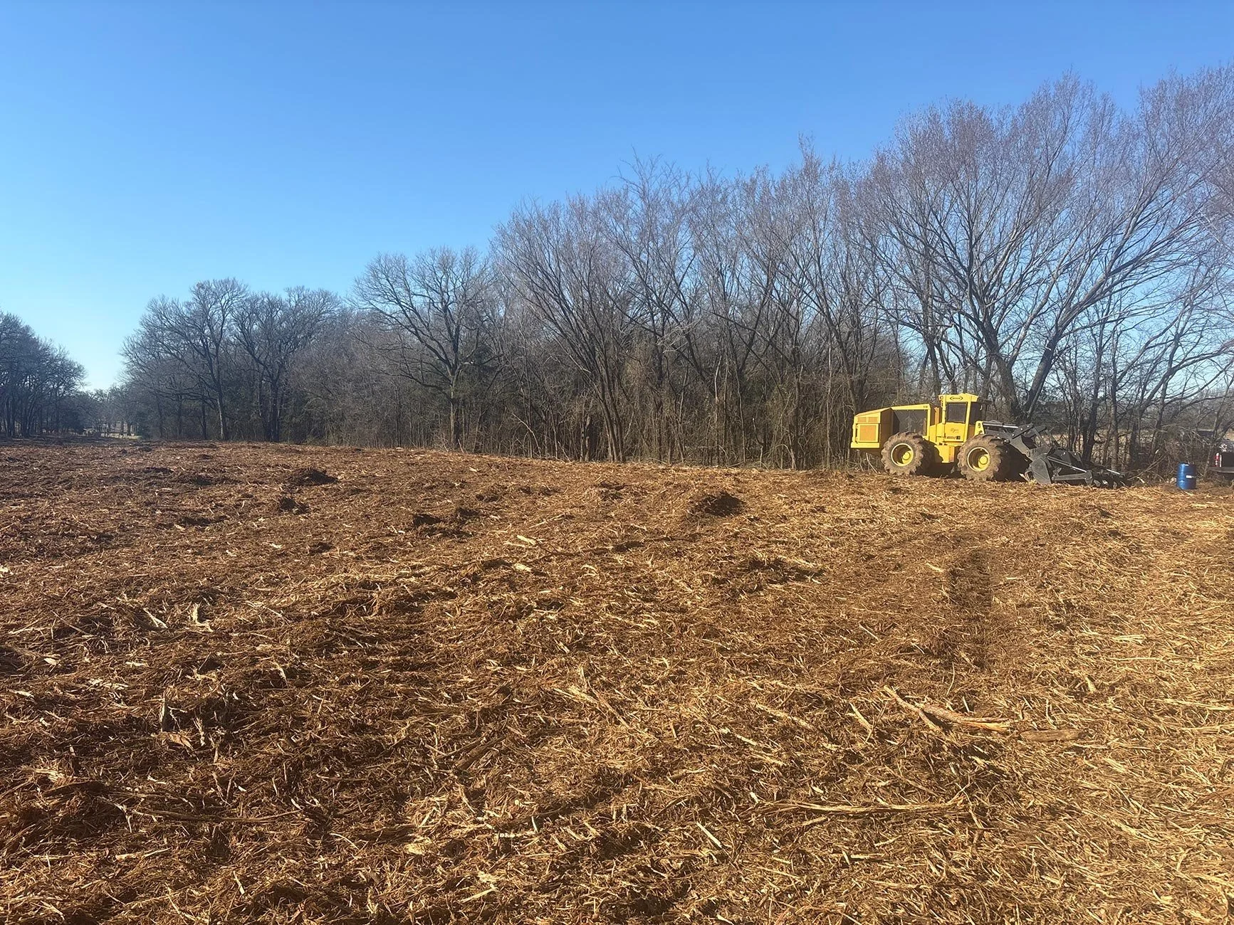 Yellow land-clearing machinery in the background of a freshly mulched field