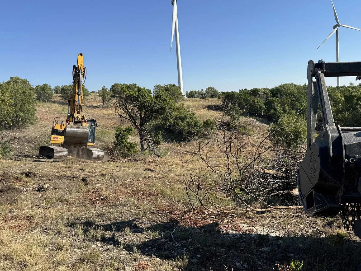 Two pieces of heavy machinery on uneven terrain near wind turbines