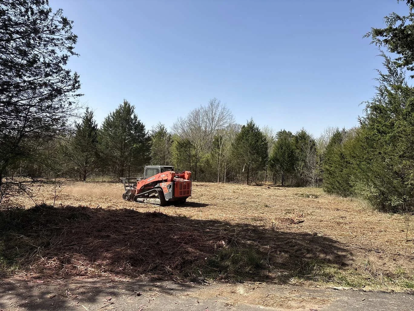 A smaller piece of land clearing machinery in a clearing among trees