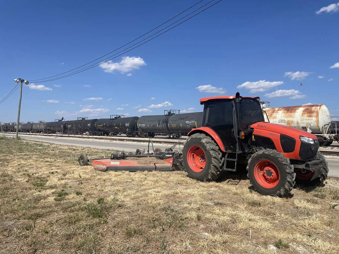 A red tractor with clearing implement next to a road and railroad