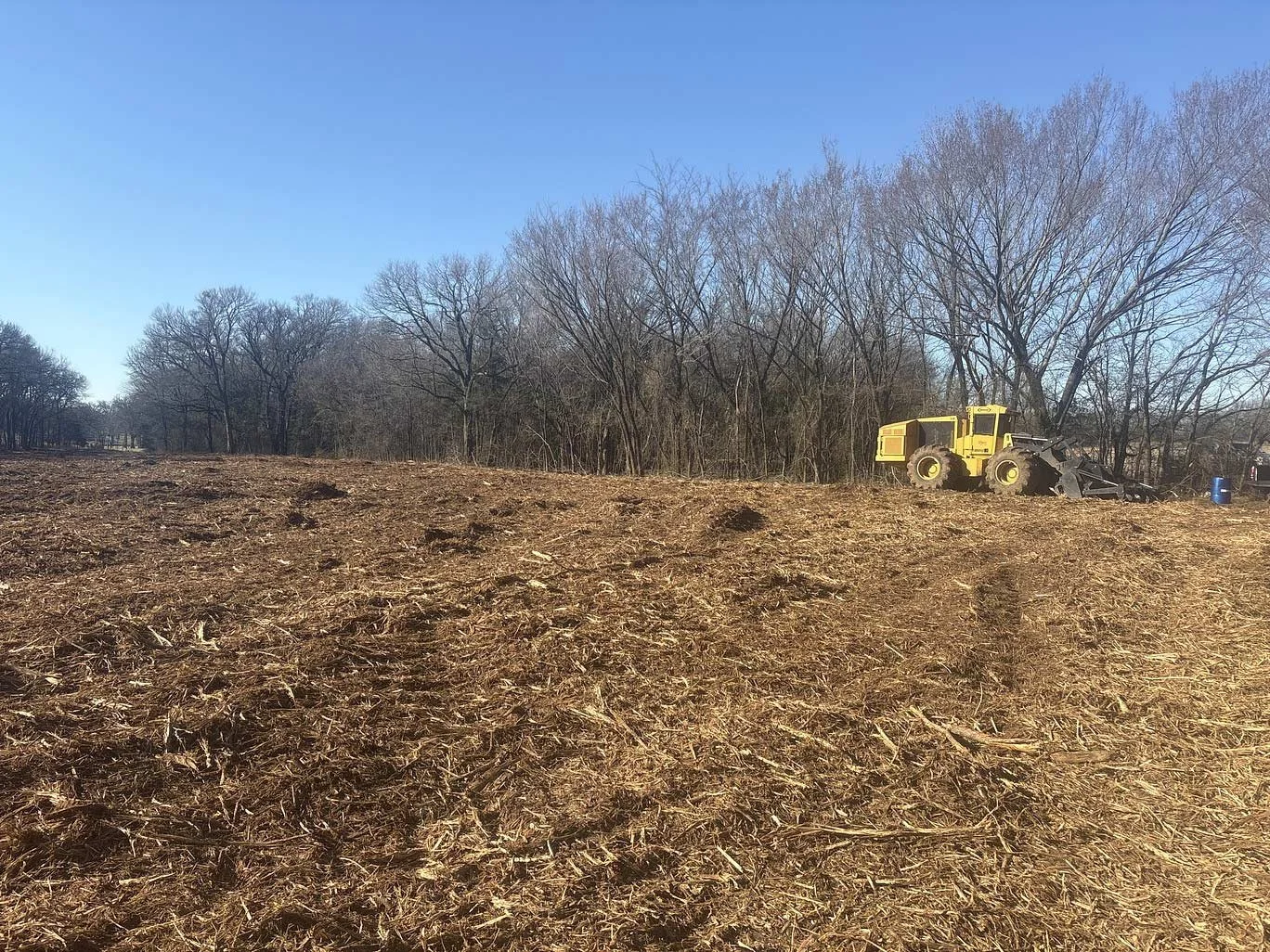 Rural property in Texas after mulching by a yellow machine in the background