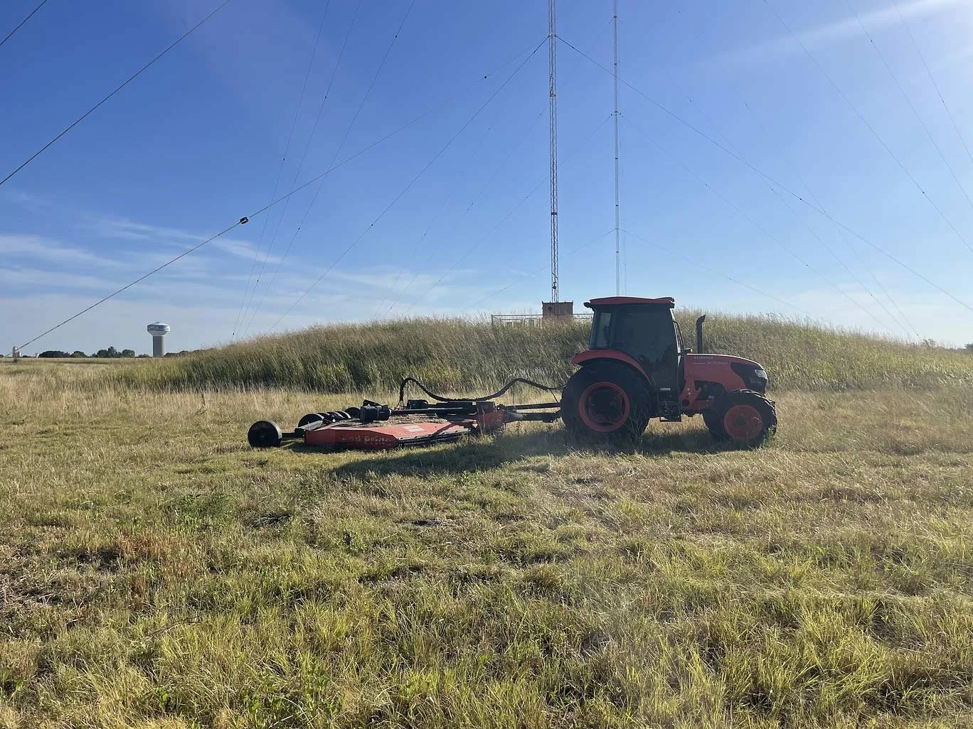 A red tractor with a land clearing implement in a grassy pasture