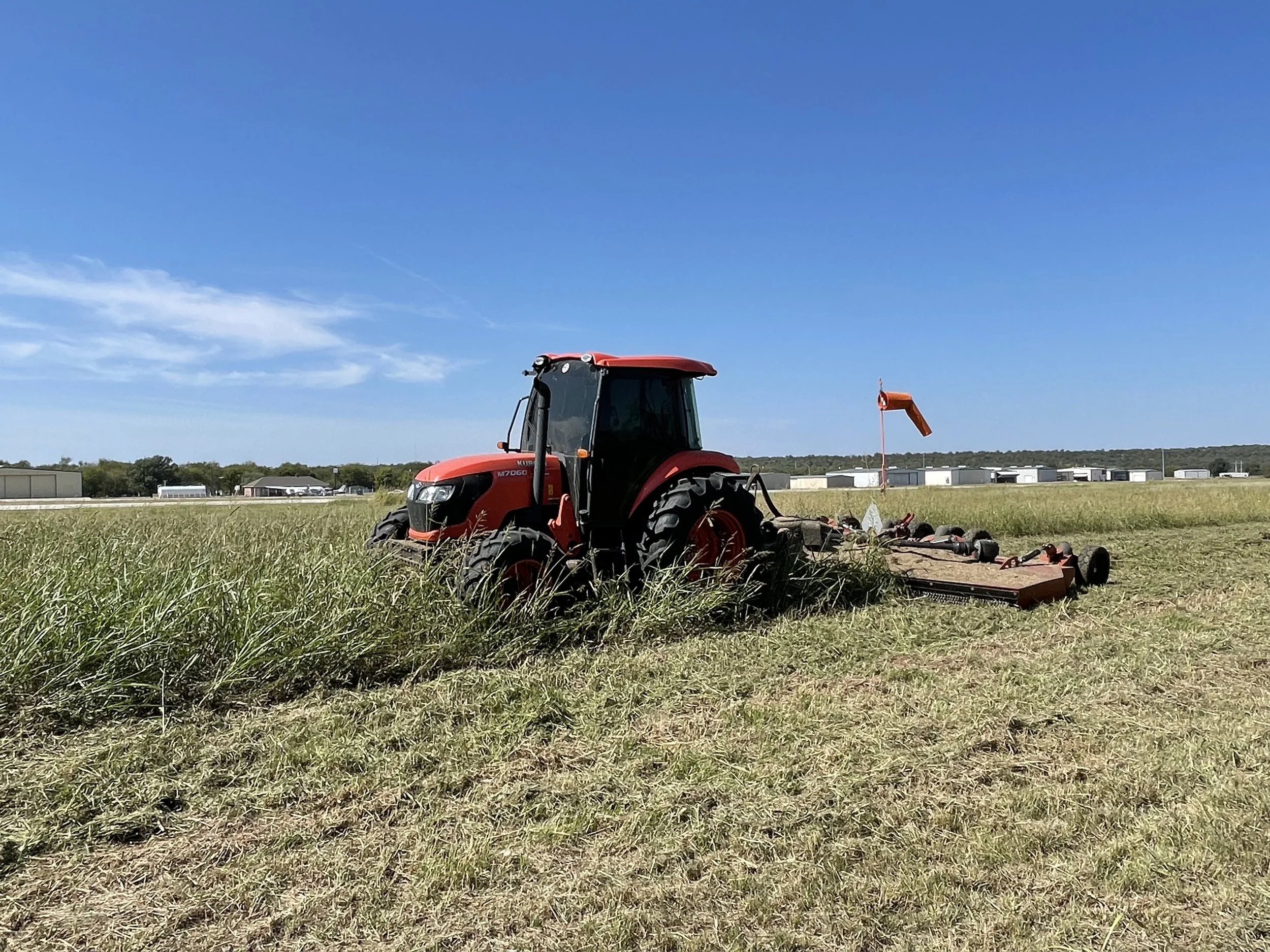 Red tractor mowing through a tall grass field