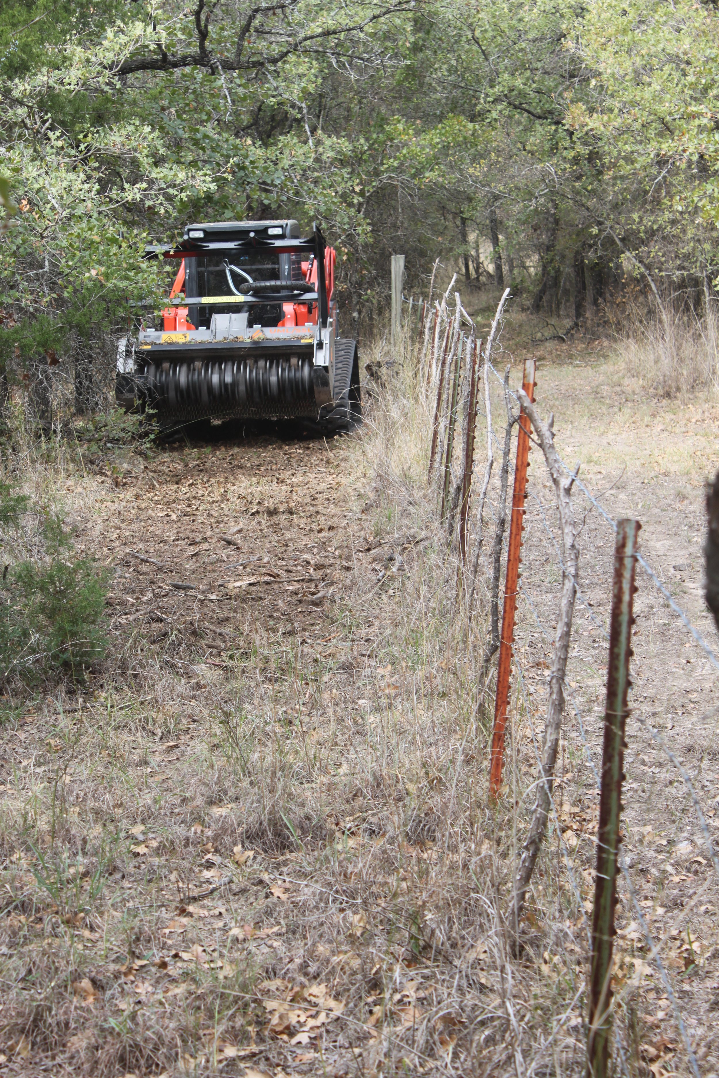 Skid-steer cutting branches along fence line