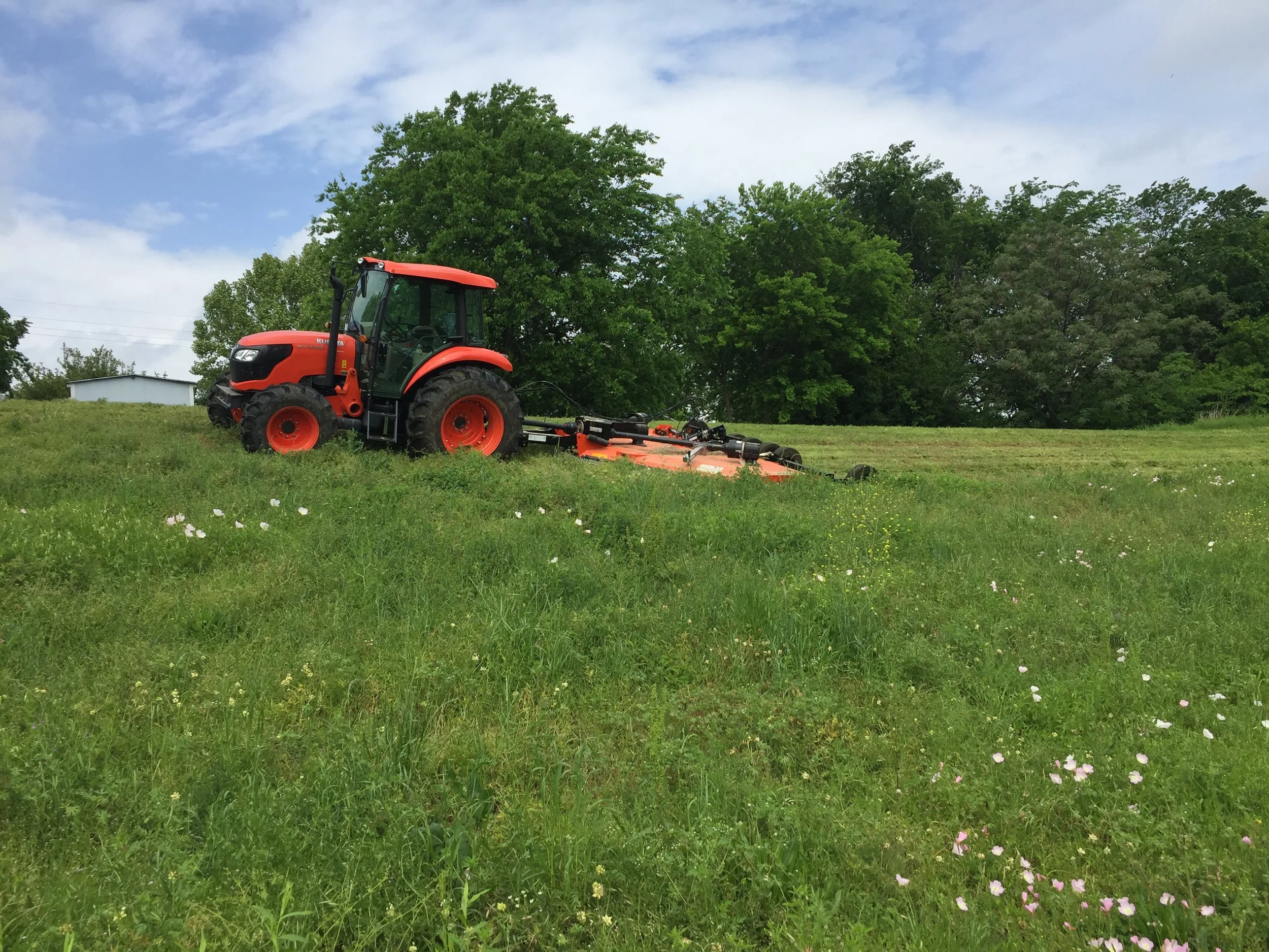 Red tractor mowing through green grass field