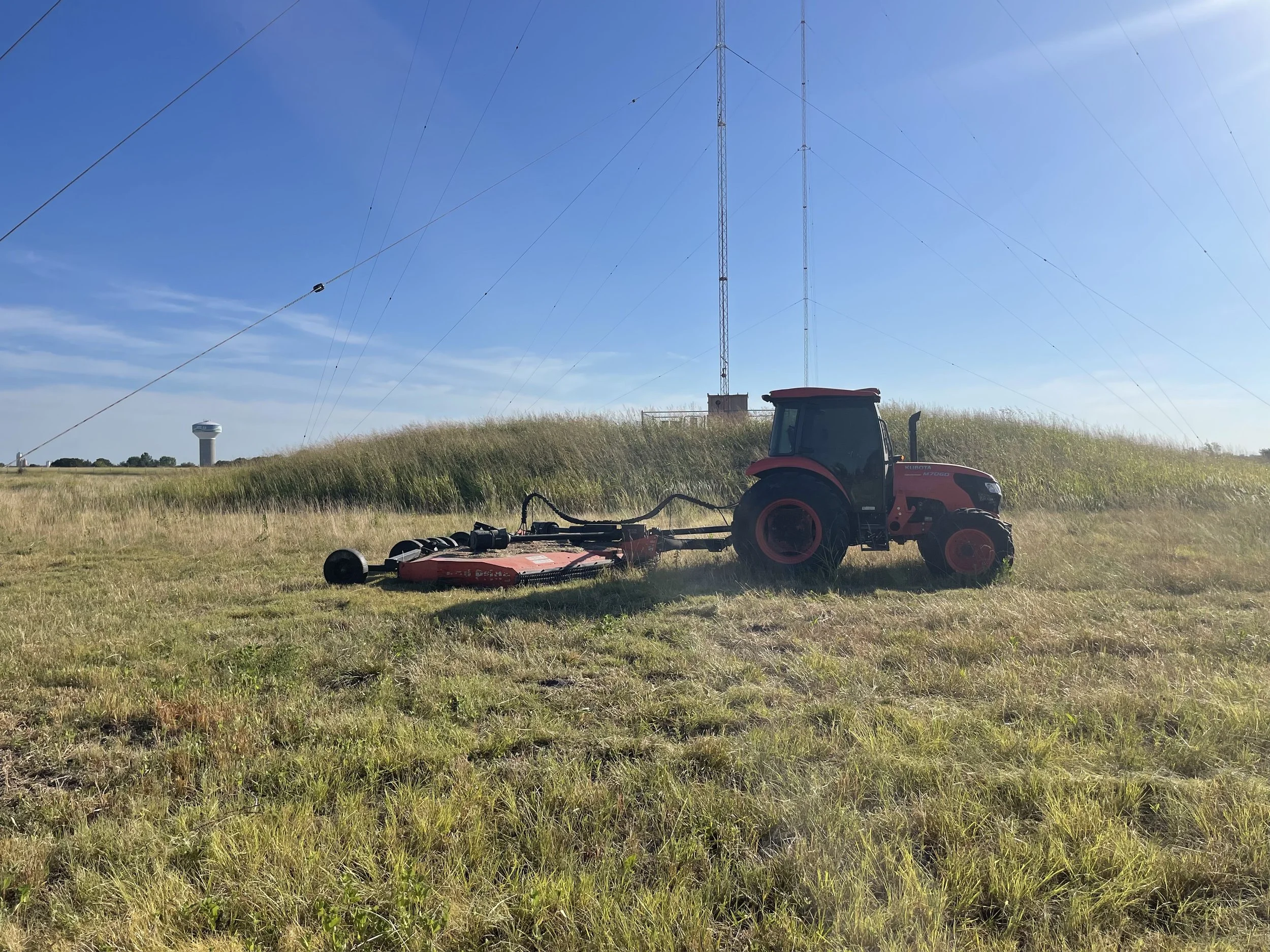 Red tractor mowing through grass field