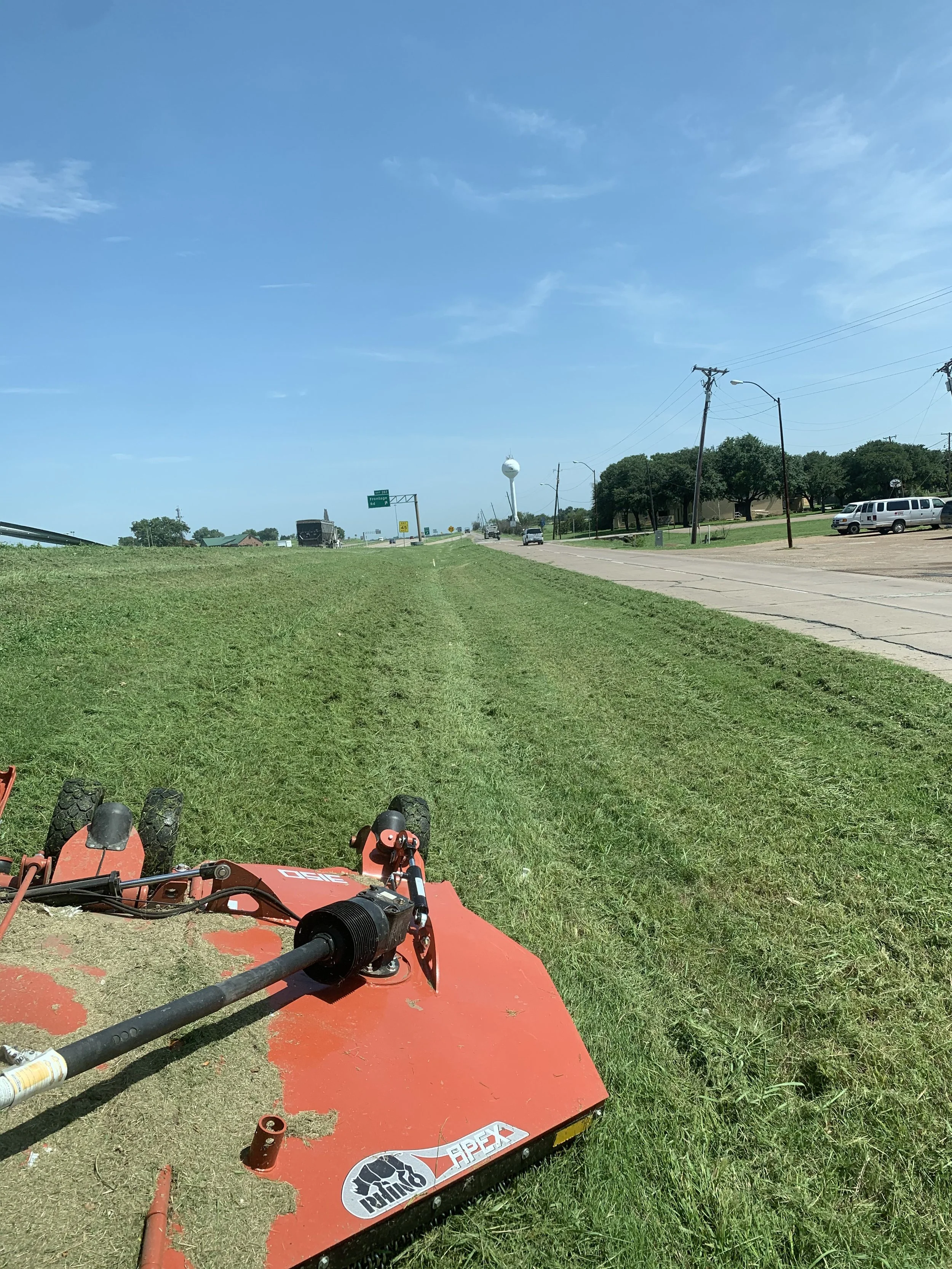 Red tractor mowing field beside road