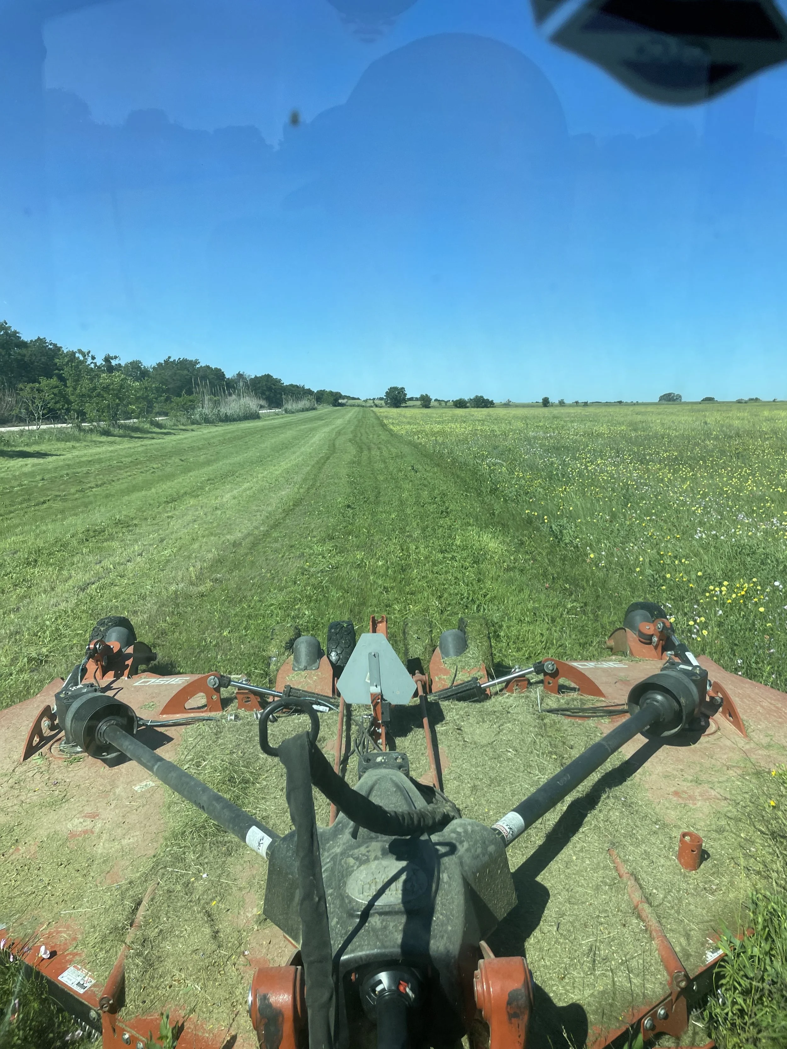 Red tractor mowing through grass field