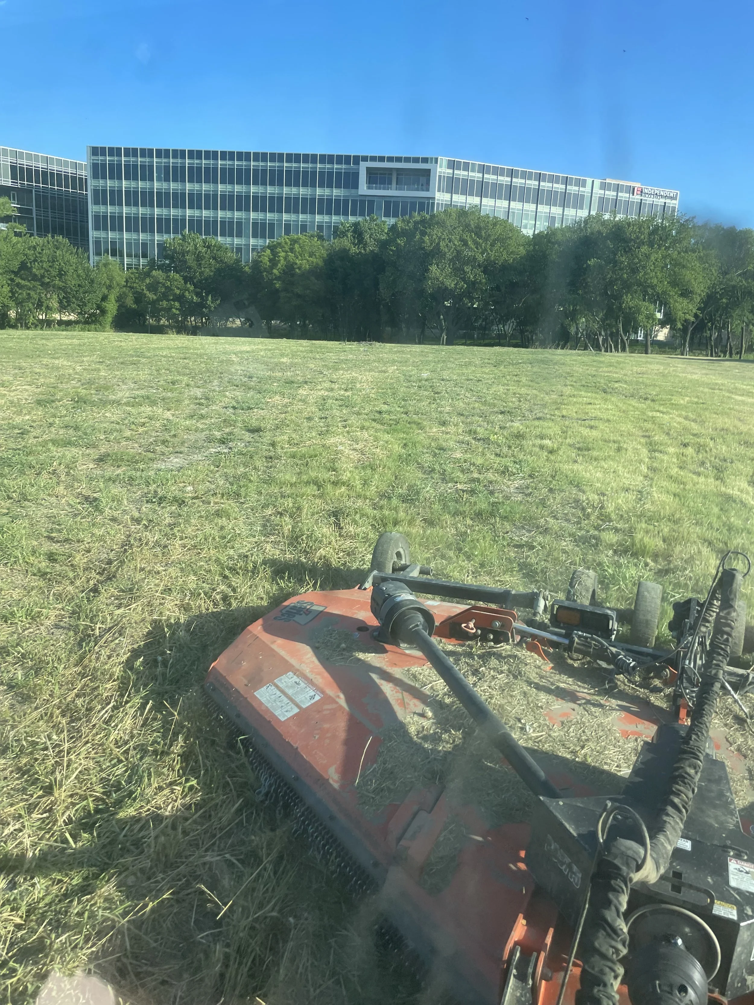 Red tractor mowing through grass field