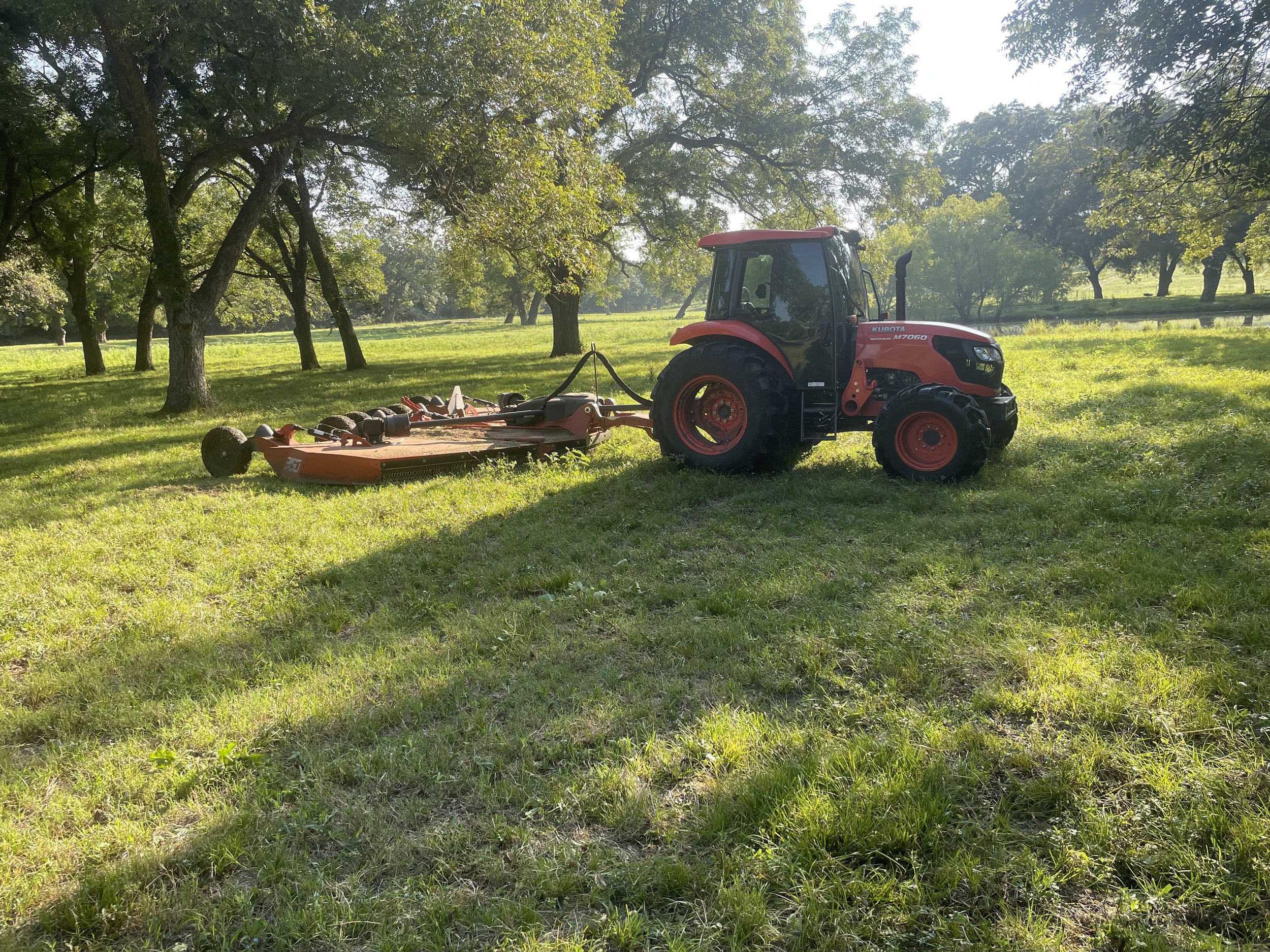 Red tractor mowing on green field
