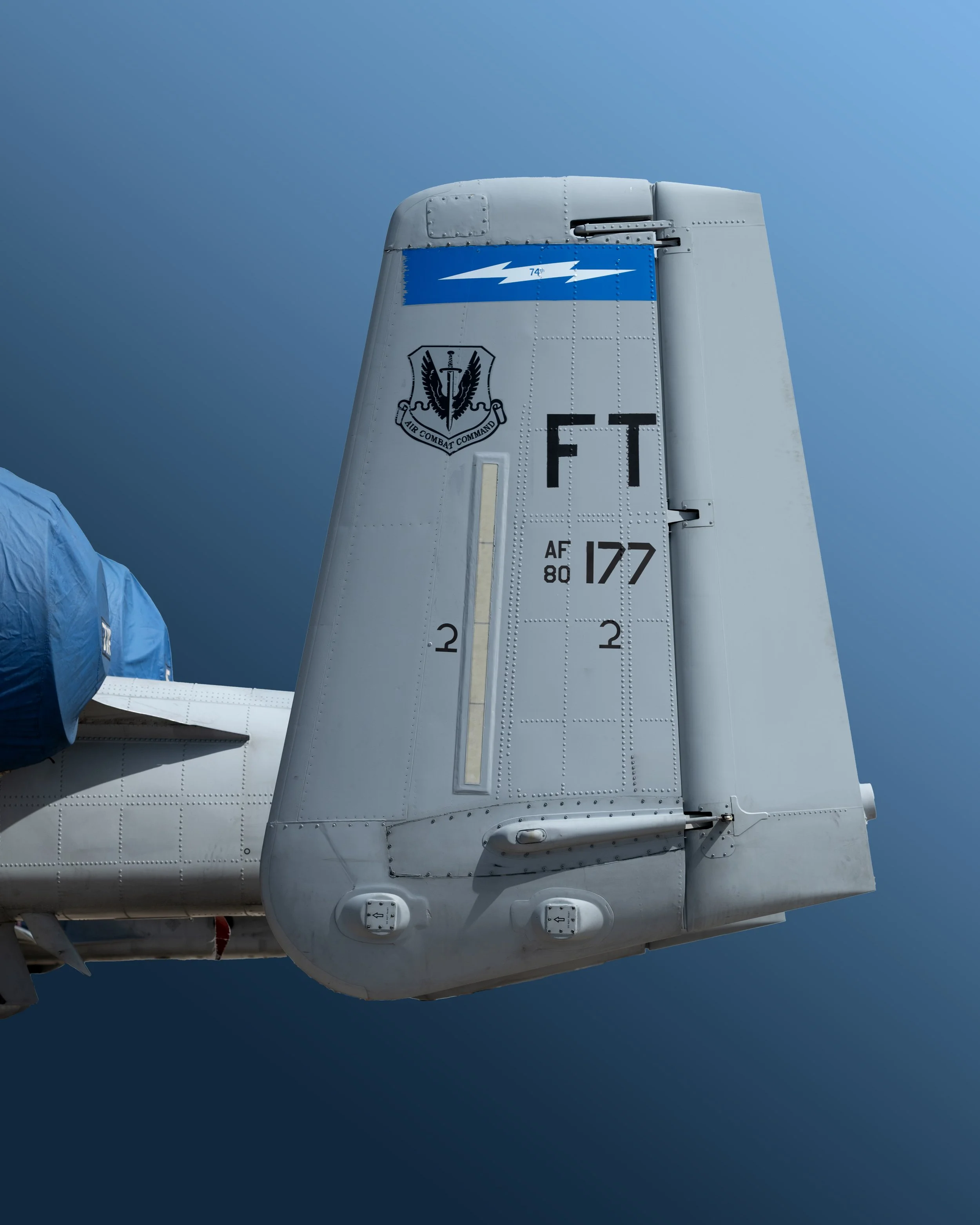 Close-up of the tail of an A-10 Thunderbolt featuring the Air Combat Command emblem and various markings, with a clear blue background.