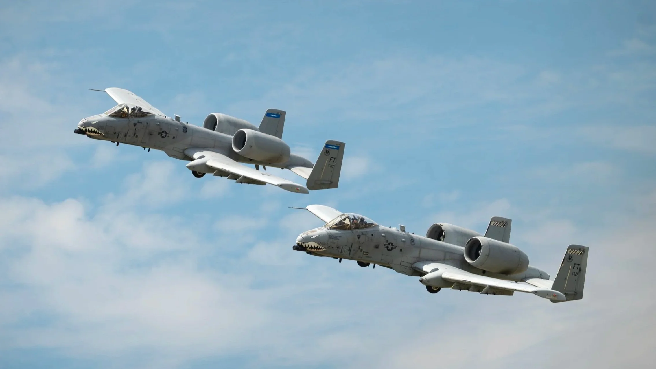Two US military A-10 Thunderbolt aircraft flying in formation under a partly cloudy sky.