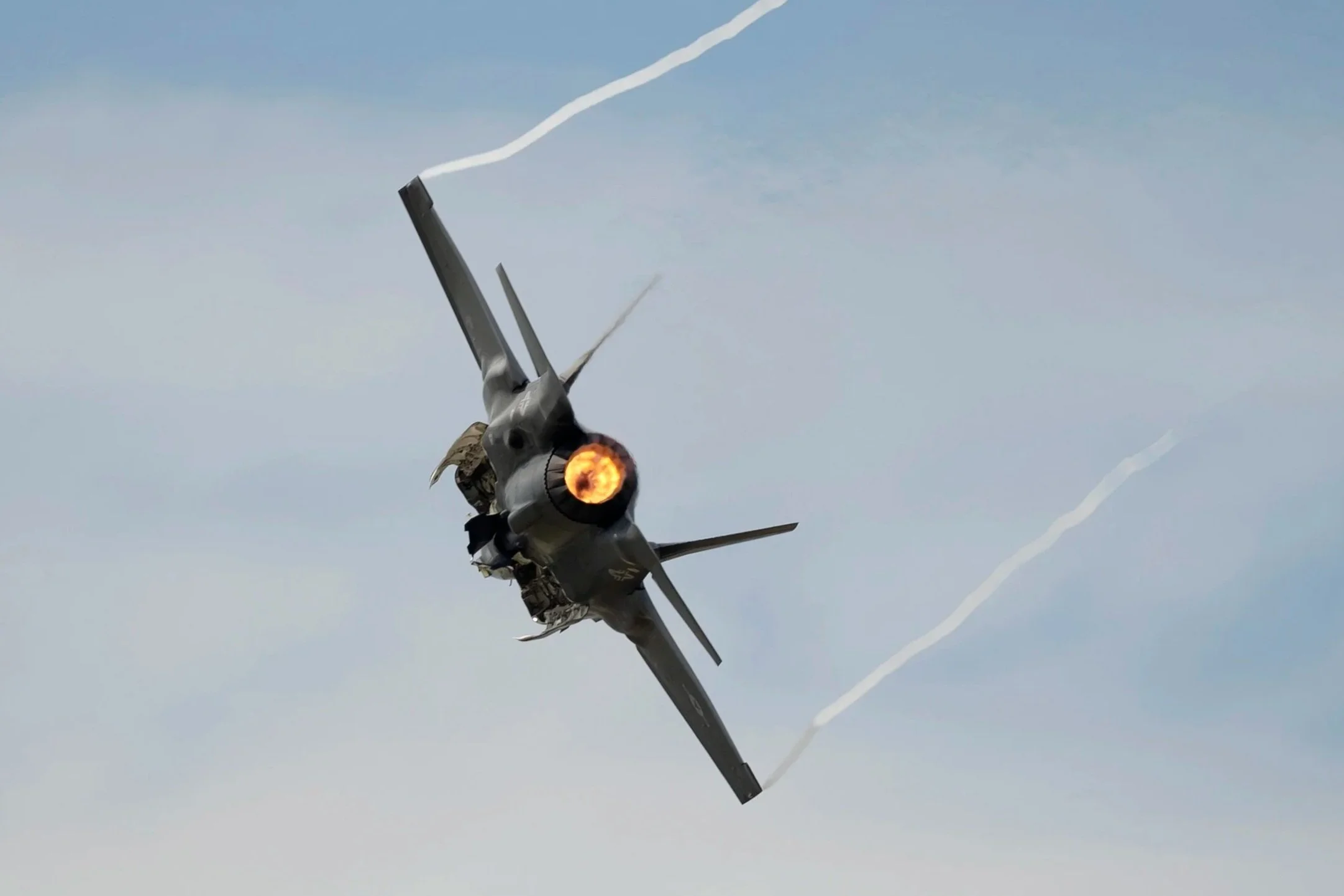 An F-35 Lighting in mid-air with afterburner firing, leaving vapor trails behind in blue sky.