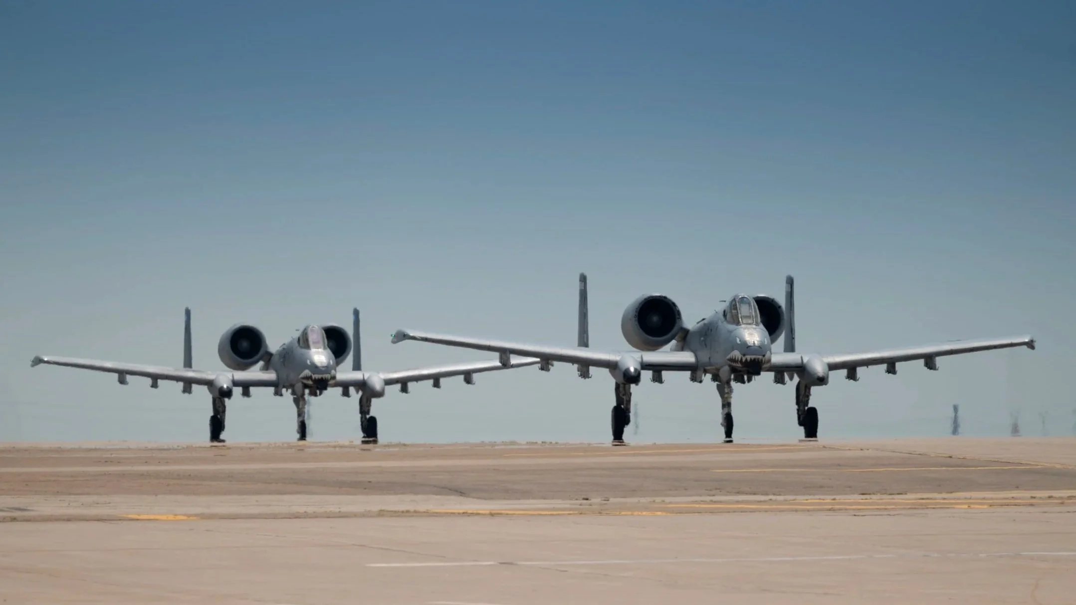 Two A-10 Thunderbolts on the runway with shark faces painted on their noses.
