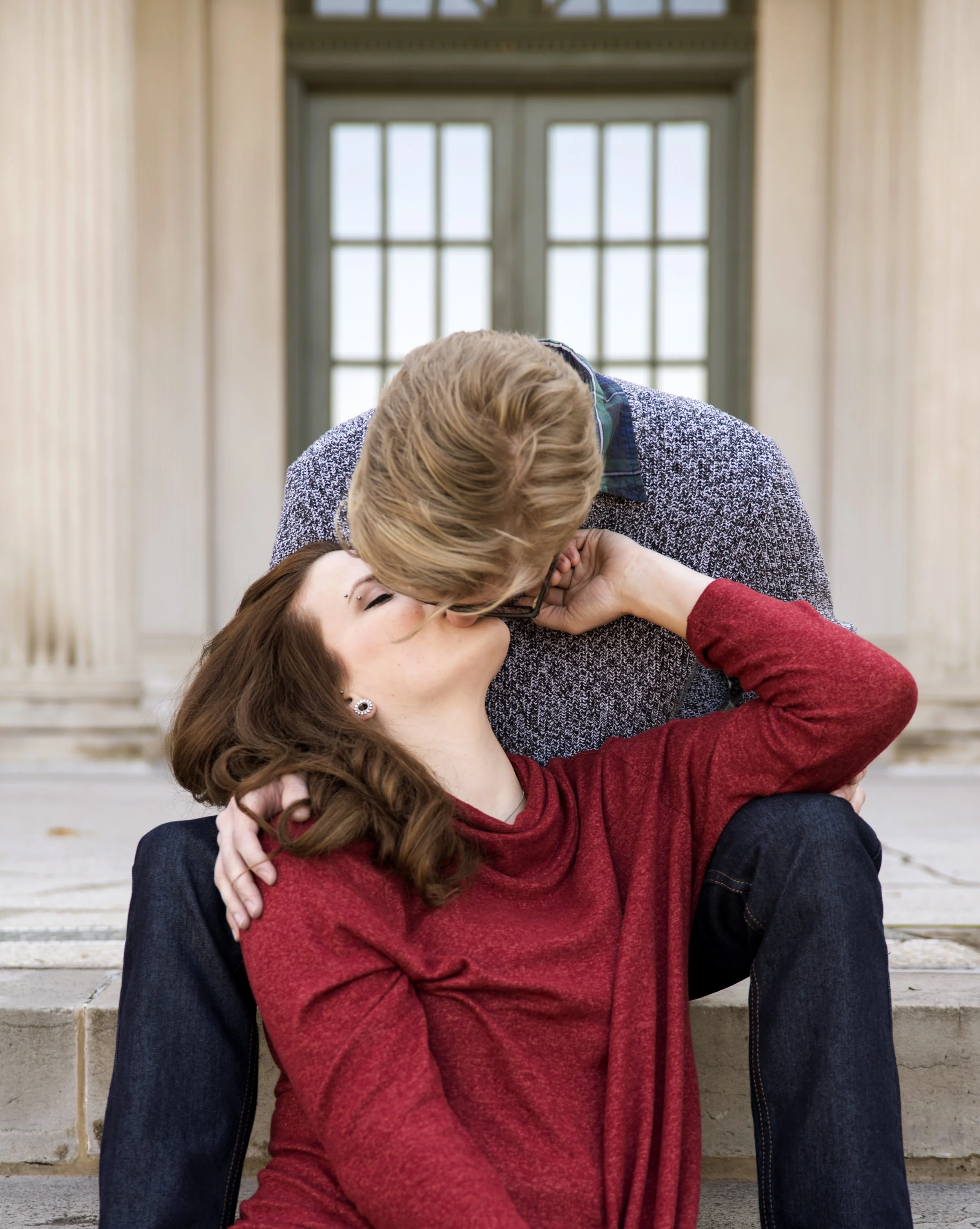 A couple sharing a kiss on steps in front of a building with large windows.