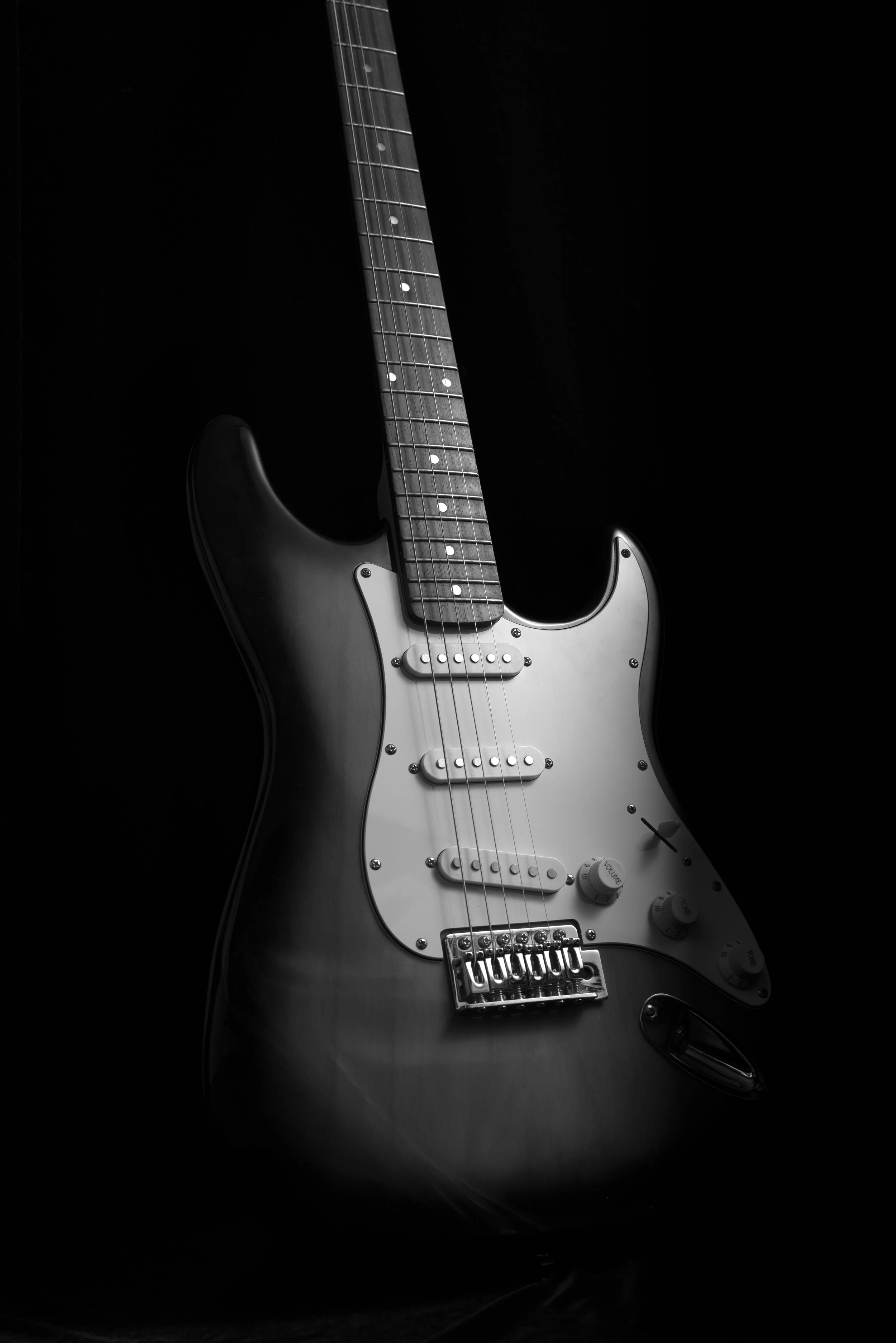 Black and white electric guitar with a sunburst finish, white pickguard, and multiple control knobs, set against a dark background.