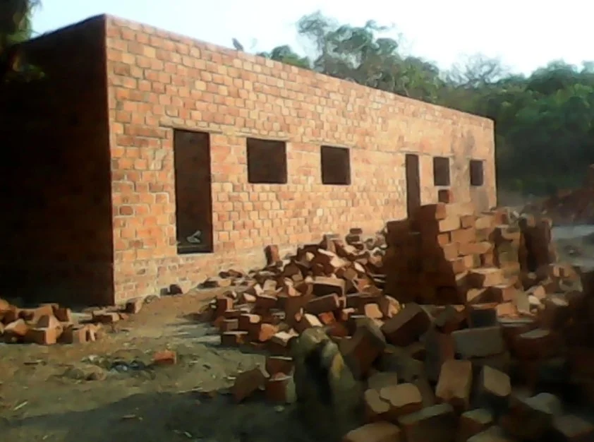 A brick building under construction with several window openings and piles of bricks in front.