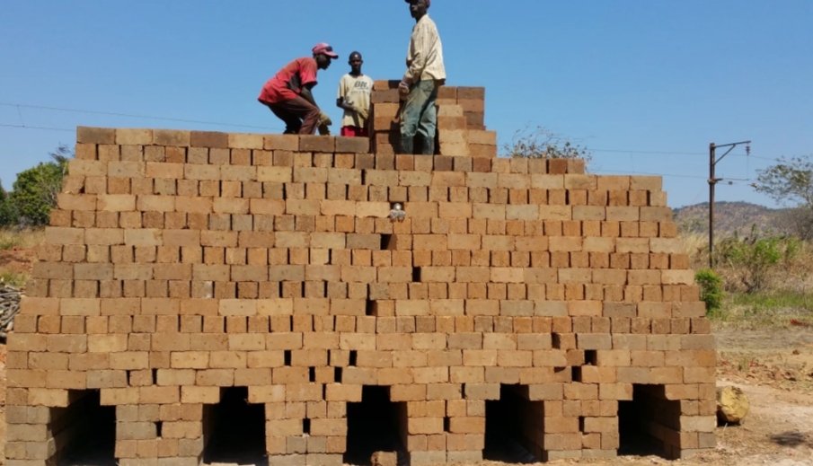 Three men building a large brick structure outdoors under a clear blue sky.