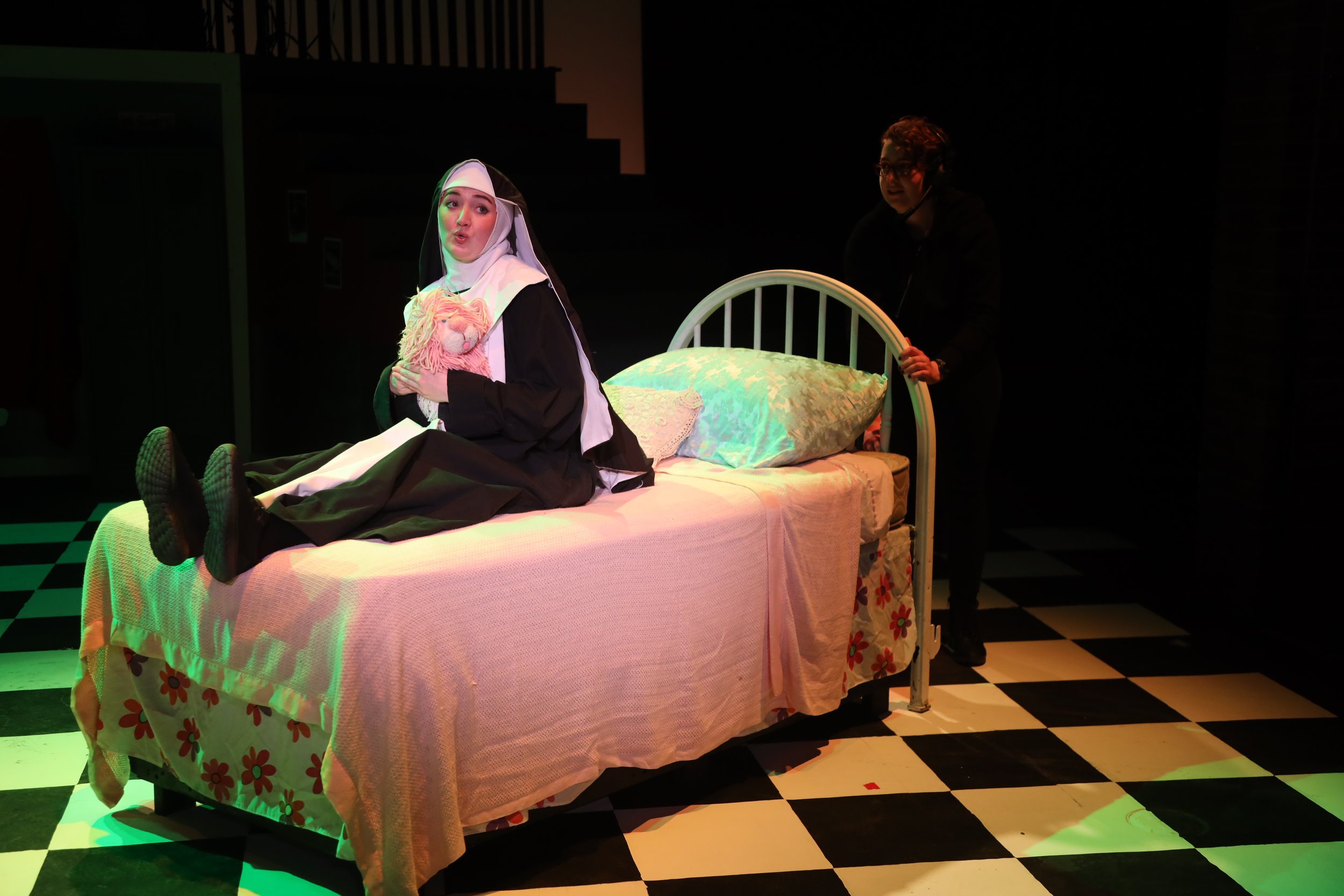 Sr. Amnesia sits on the bed from Grease