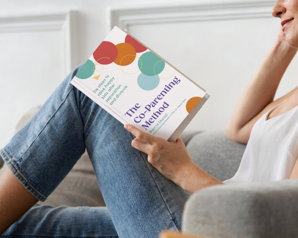 Person reading a book titled 'The Co-Parenting Method' in a cozy, well-lit room.