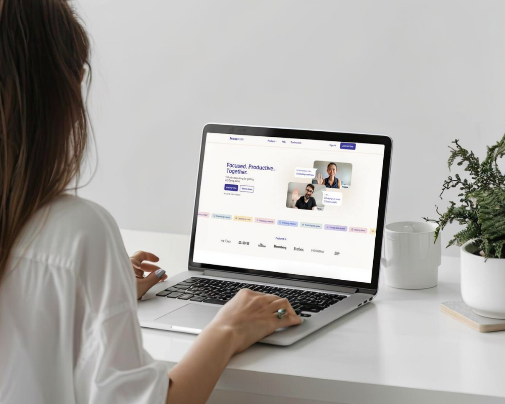 Person using a laptop at a white desk with a plant and a white cup on it.