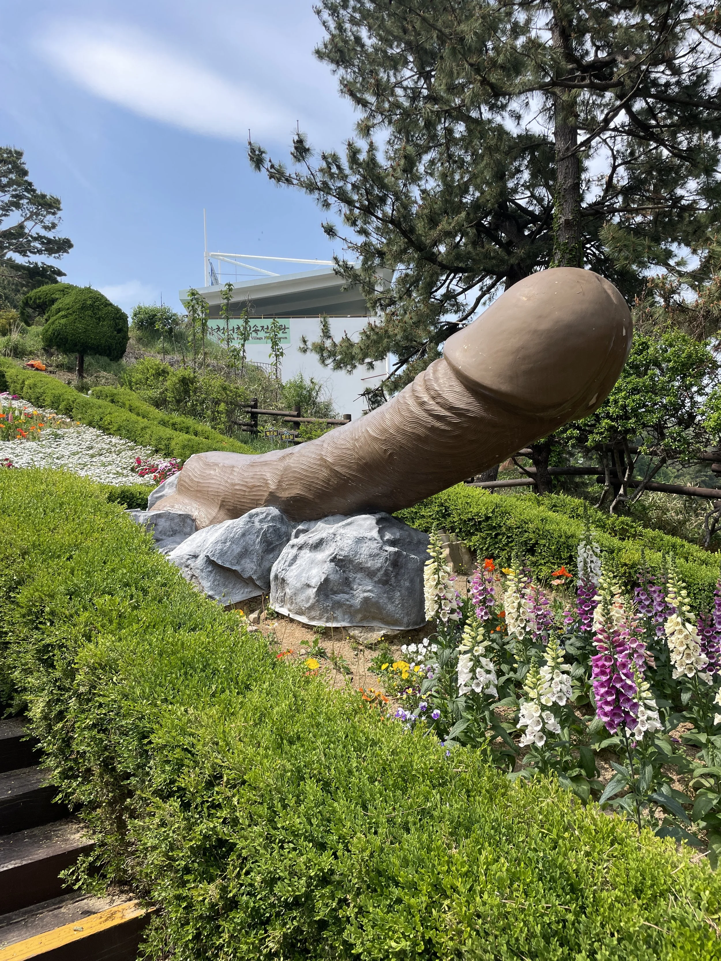 giant carved penis in the middle of a flower garden