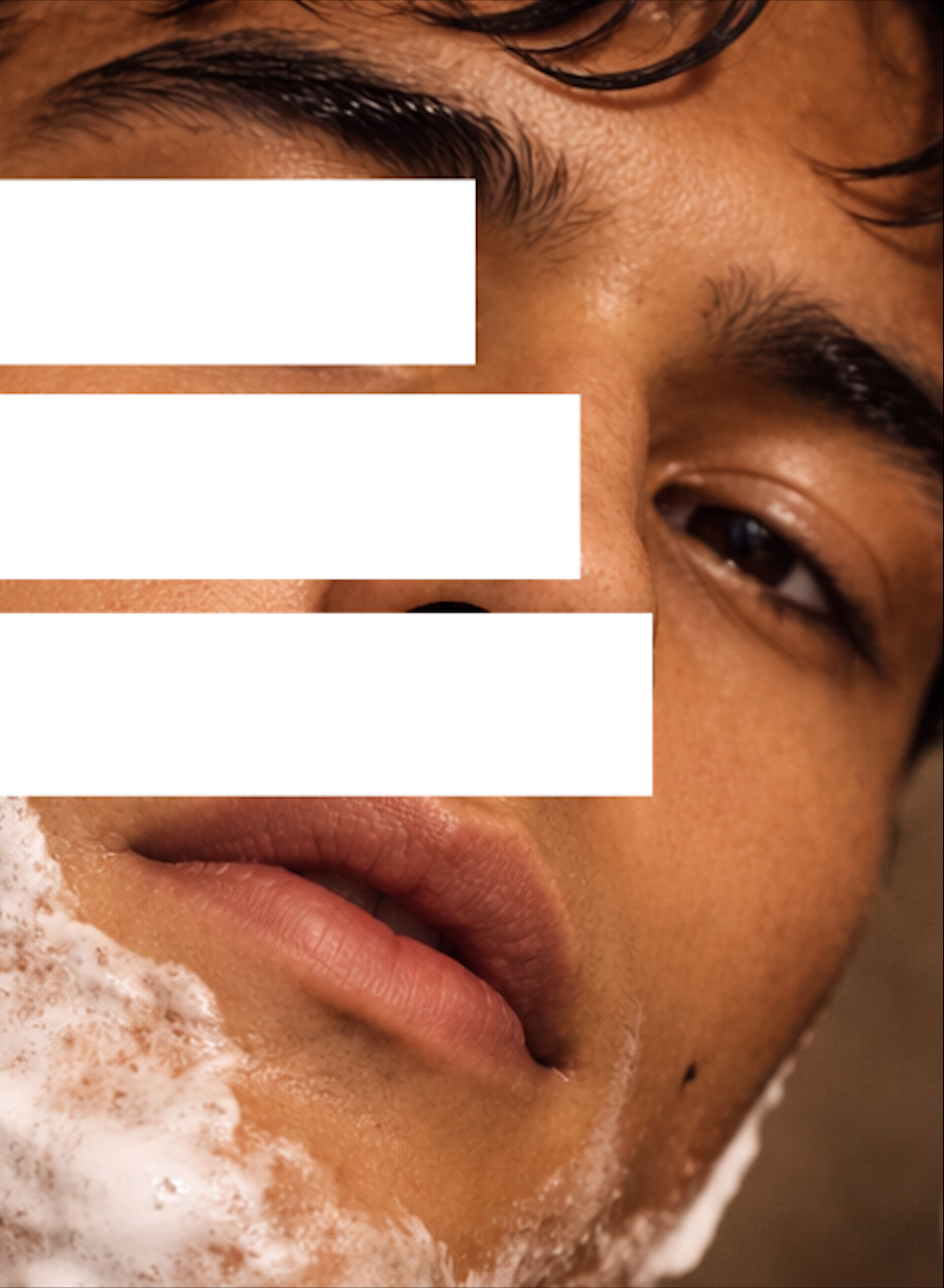 Close-up of a person's face with soap lather on the chin, revealing the skin texture, lips, and partially open eyes.