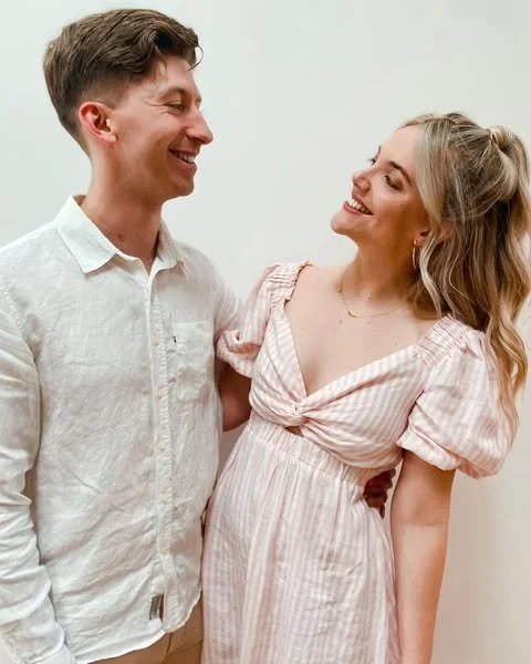 A smiling young man and woman looking at each other, standing close against a white background.