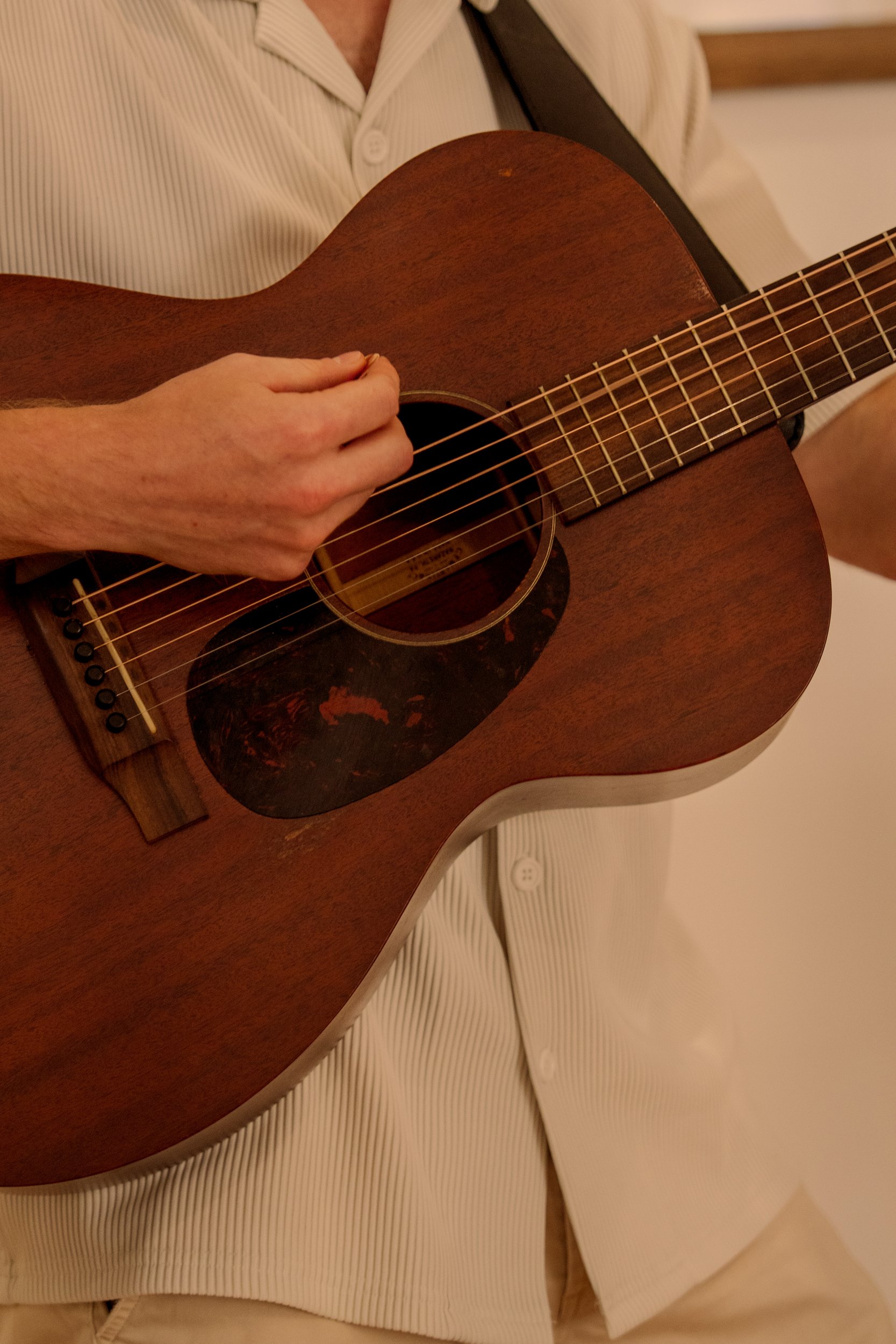 A person dressed in a light-colored, vertically striped shirt playing a brown acoustic guitar.