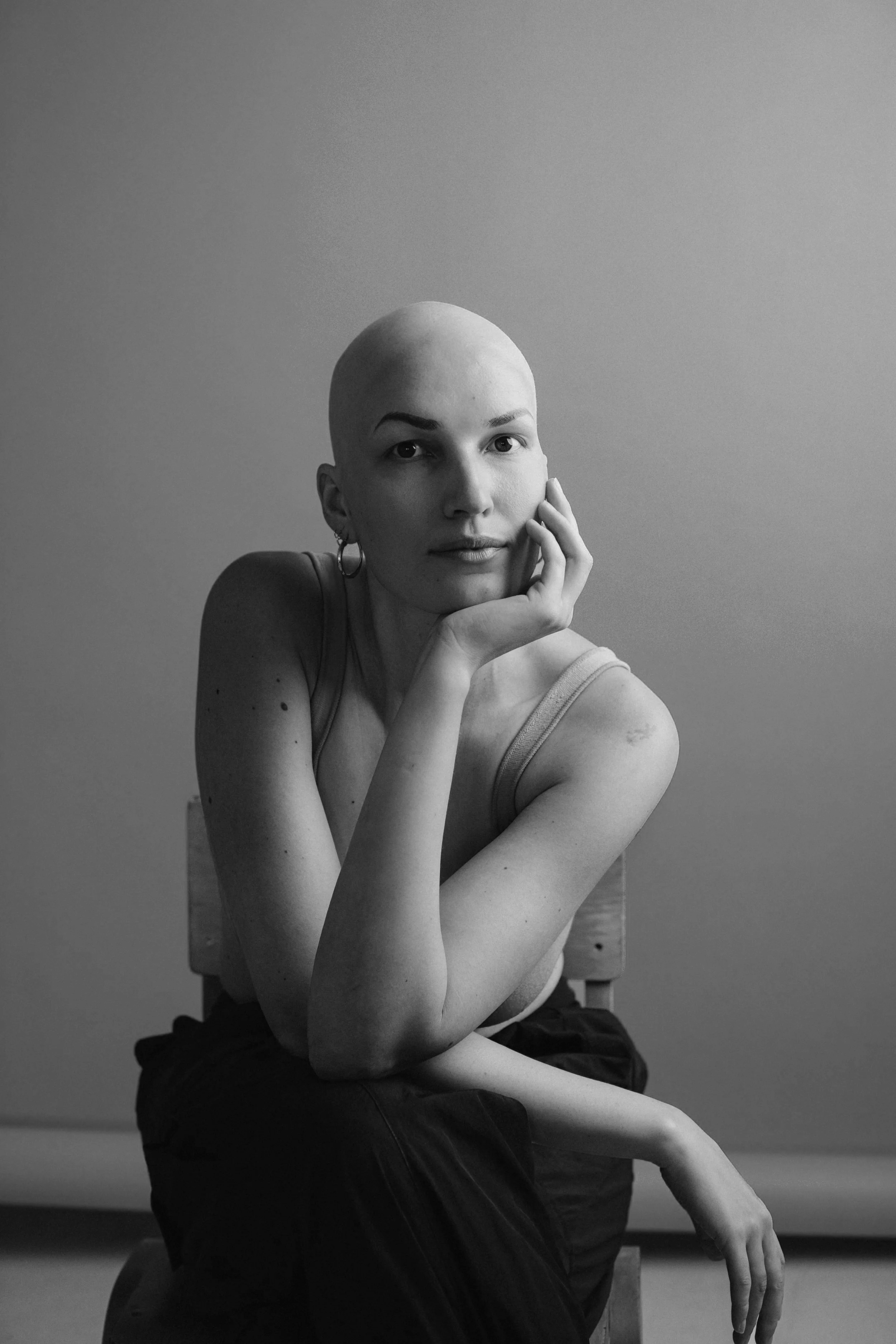 Black and white portrait of a woman with a shaved head, wearing a tank top, resting her chin on her hand. To the right, a German quote about beauty and culture, and the name Suni Ferri.