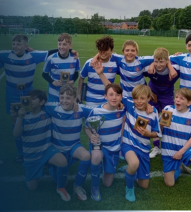 Youth soccer team in blue and white striped jerseys, some holding medals and a trophy, posing on a soccer field.