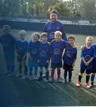 A coach and seven young children in blue sports uniforms standing on a soccer field.
