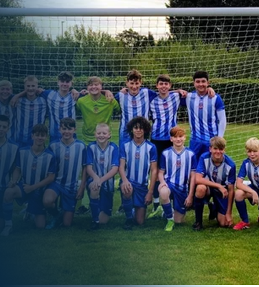 A youth soccer team in blue and white striped jerseys posing on the field with their coach in front of a goal.