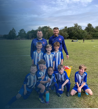 Group of young soccer players in blue and white uniforms with two coaches on a grassy field during daytime