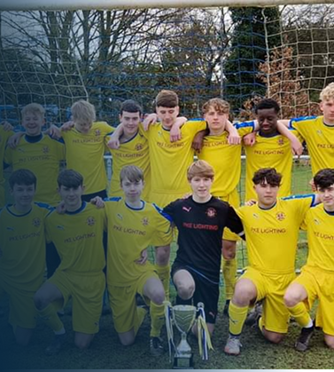 Youth football team in yellow kits posing for a team photo on a football pitch with a trophy in front.