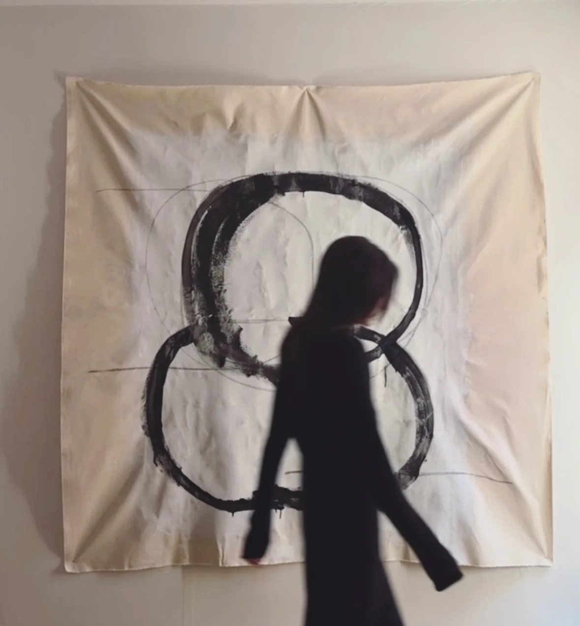 Person walking past a large abstract black and white painting with circular shapes on a wall.