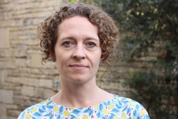 A woman called Stella smiling in front of a brick wall.