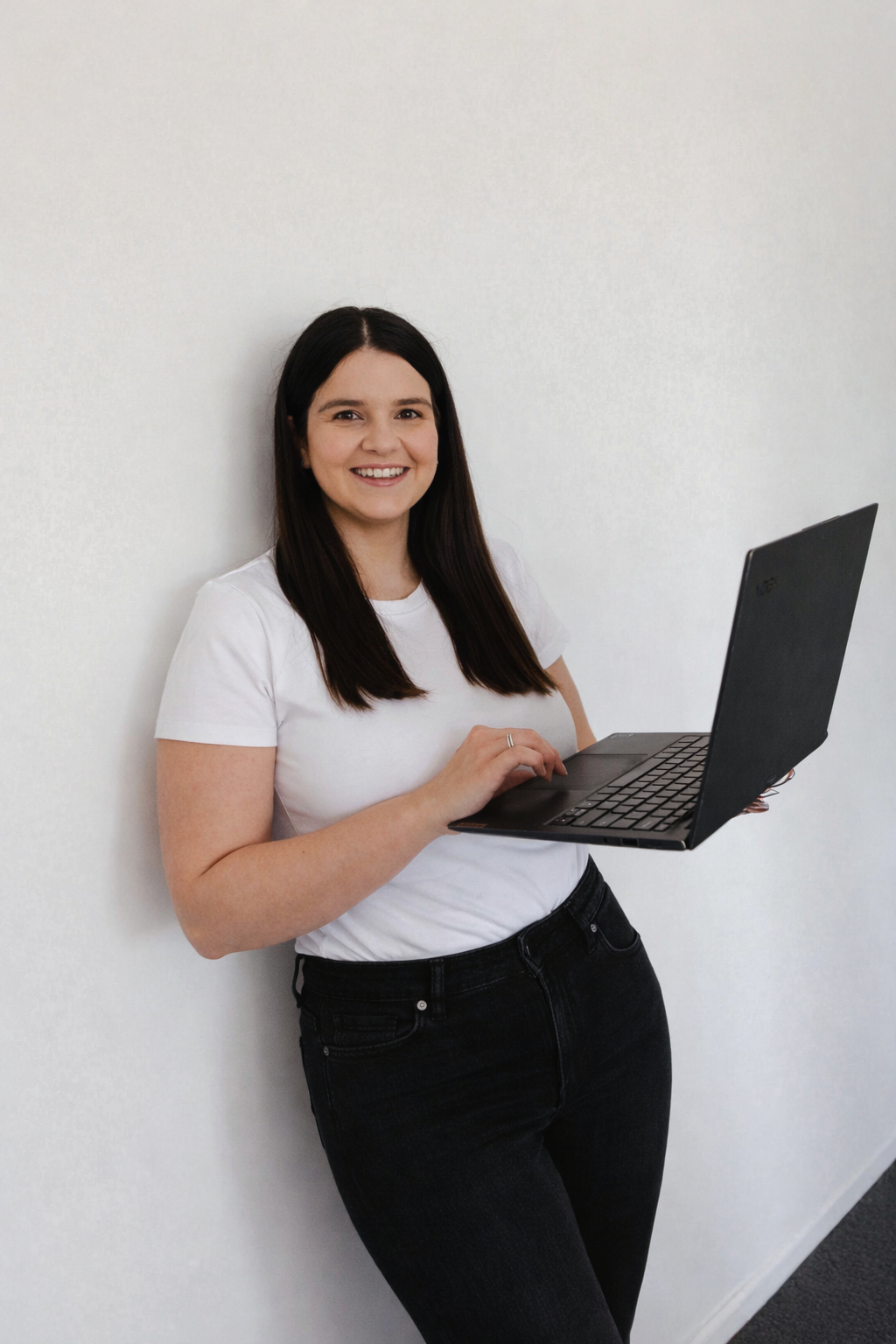 Expert Human Resources Consultant standing against a white wall with a laptop and smiling.