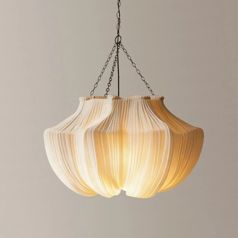Sculptural beige fabric chandelier with a softly glowing pleated shade suspended from dark metal chains.