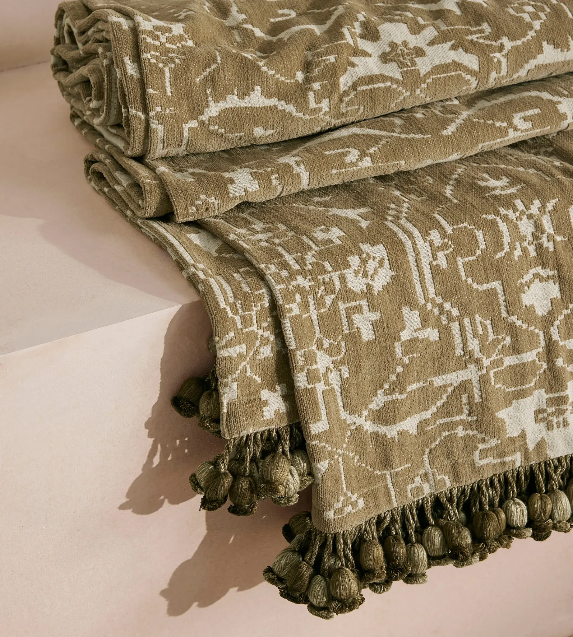 Silvanus Bedspread by Soho Home, featuring stylized botanical motifs in warm olive and ivory with a decorative tassel border. Its textured weave and earthy palette add depth and collected character, bringing a rich finishing layer to a softly styled 