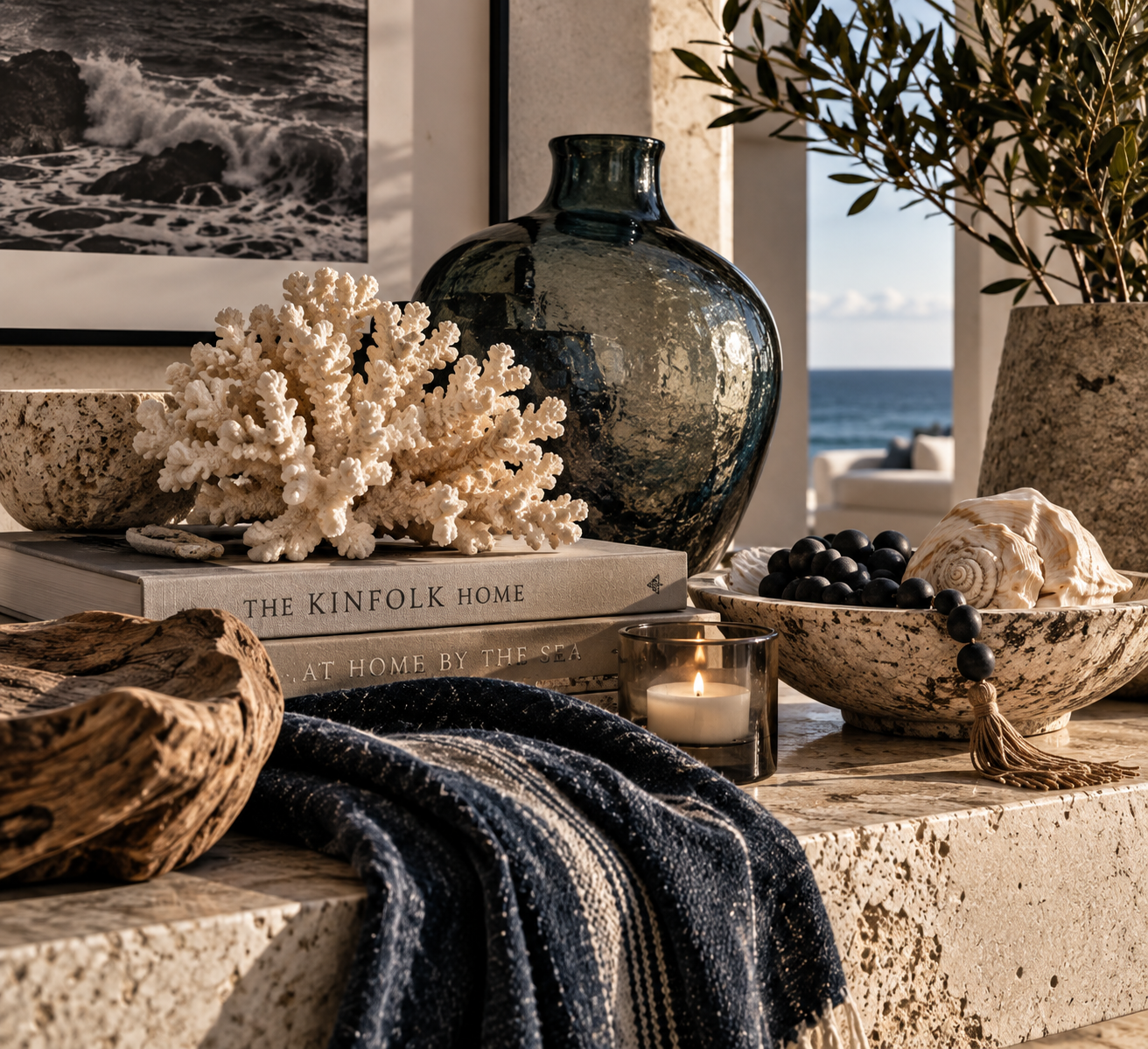 Coastal material study with sculptural white coral, smoky blue glass, limestone, weathered wood, shells and an indigo textile overlooking the ocean.