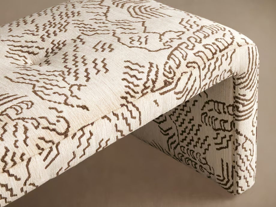 A cream upholstered bench with warm brown geometric patterning, a softly tufted seat, and a clean waterfall silhouette. Its textured fabric adds depth and character, while the neutral palette brings a quiet balance to richer colors and collected furn