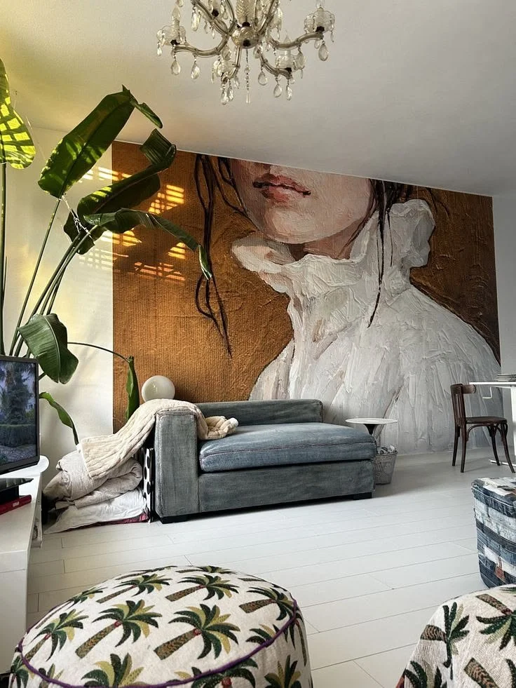 Oversized portrait of a woman in a cream ruffled blouse above a blue-gray chaise, surrounded by leafy plants and layered textiles.