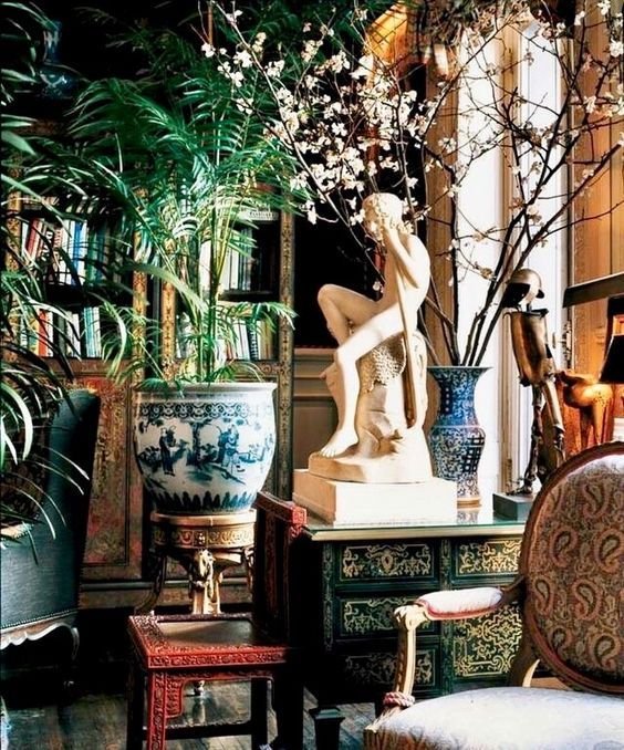 Collected interior with a classical white sculpture, blue-and-white ceramic vessels, chinoiserie furniture, and lush palms.