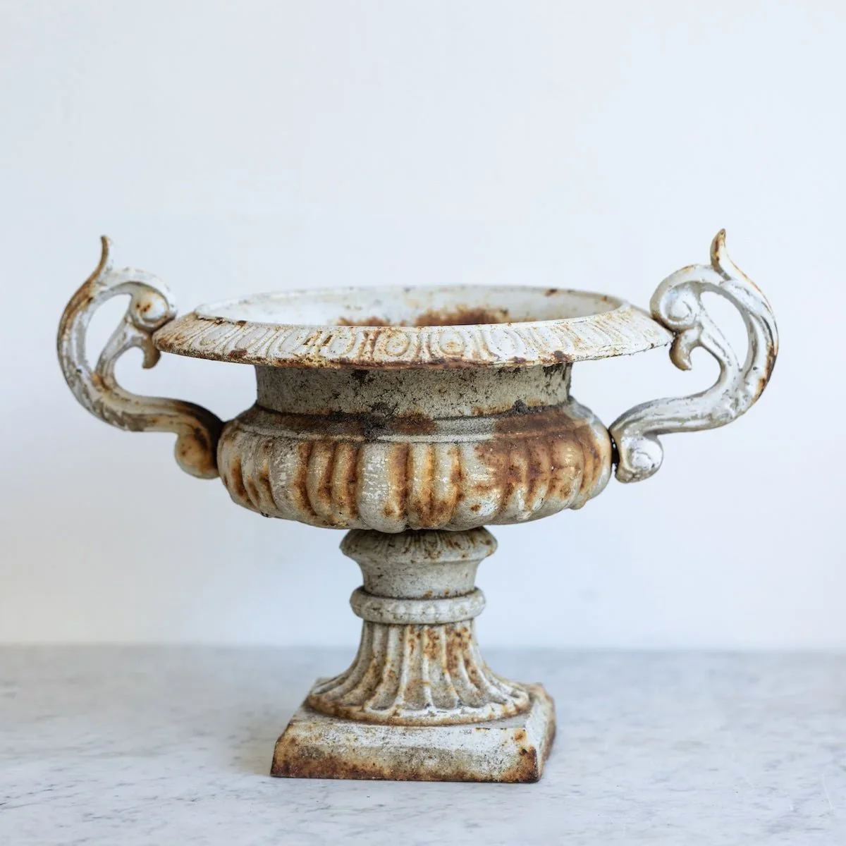 Vintage Cast Iron Garden Urn | Elsie Green

Discovered at a flea market in Avignon, France, this vintage cast-iron urn brings a sense of history and understated European charm. Its chipped ivory finish, natural rust patina, and ornate detailing celeb