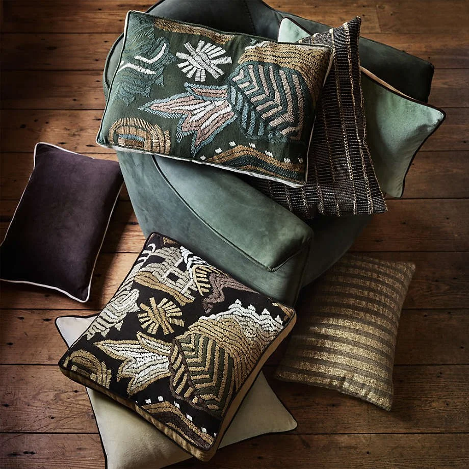 Pillows by Jeremiah Brent for Crate & Barrel. Rich greens, muted plum, embroidered motifs, and woven stripes bring layered texture and inviting warmth to a room.
