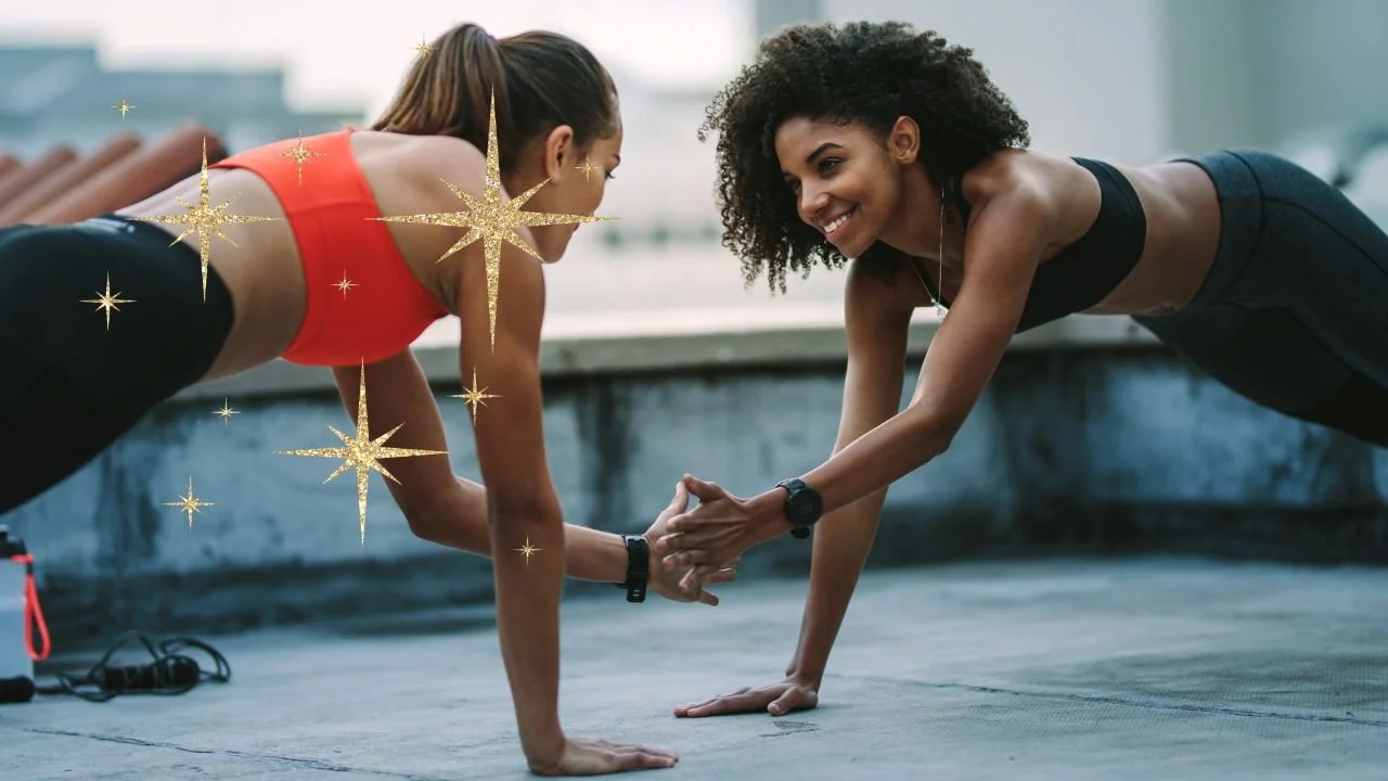 Two women engaging in partner push-ups outdoors, smiling and holding hands, with gym equipment nearby and city buildings in the background. Glitter effect overlay.
