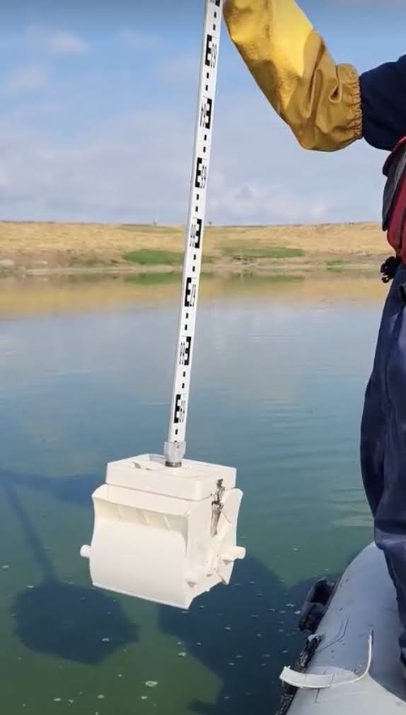 Person holding a sludge measurement device over a tailings pond