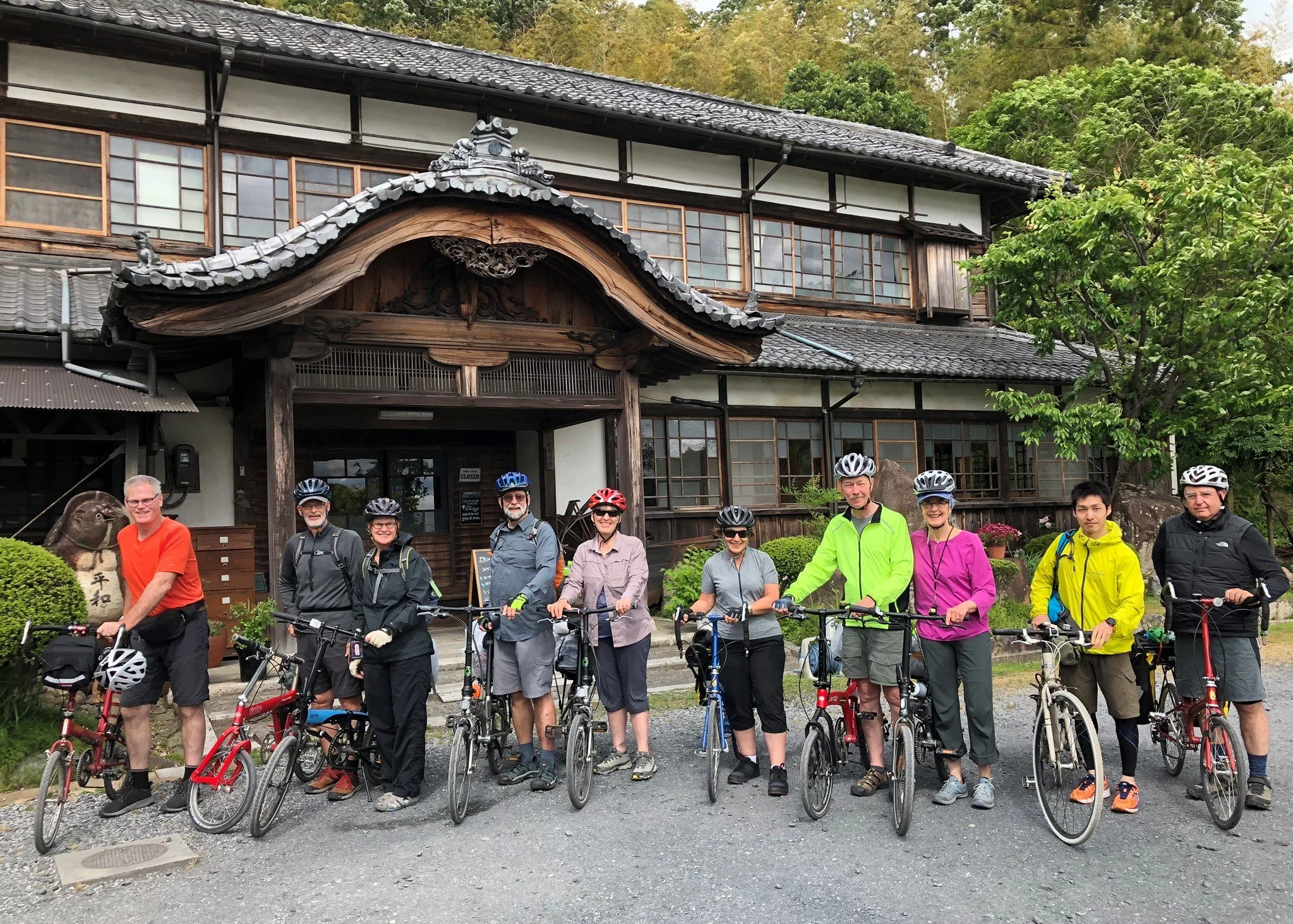 8 bicyclists in colorful athletic gear stand outside hostel with beautiful Japanese architecture