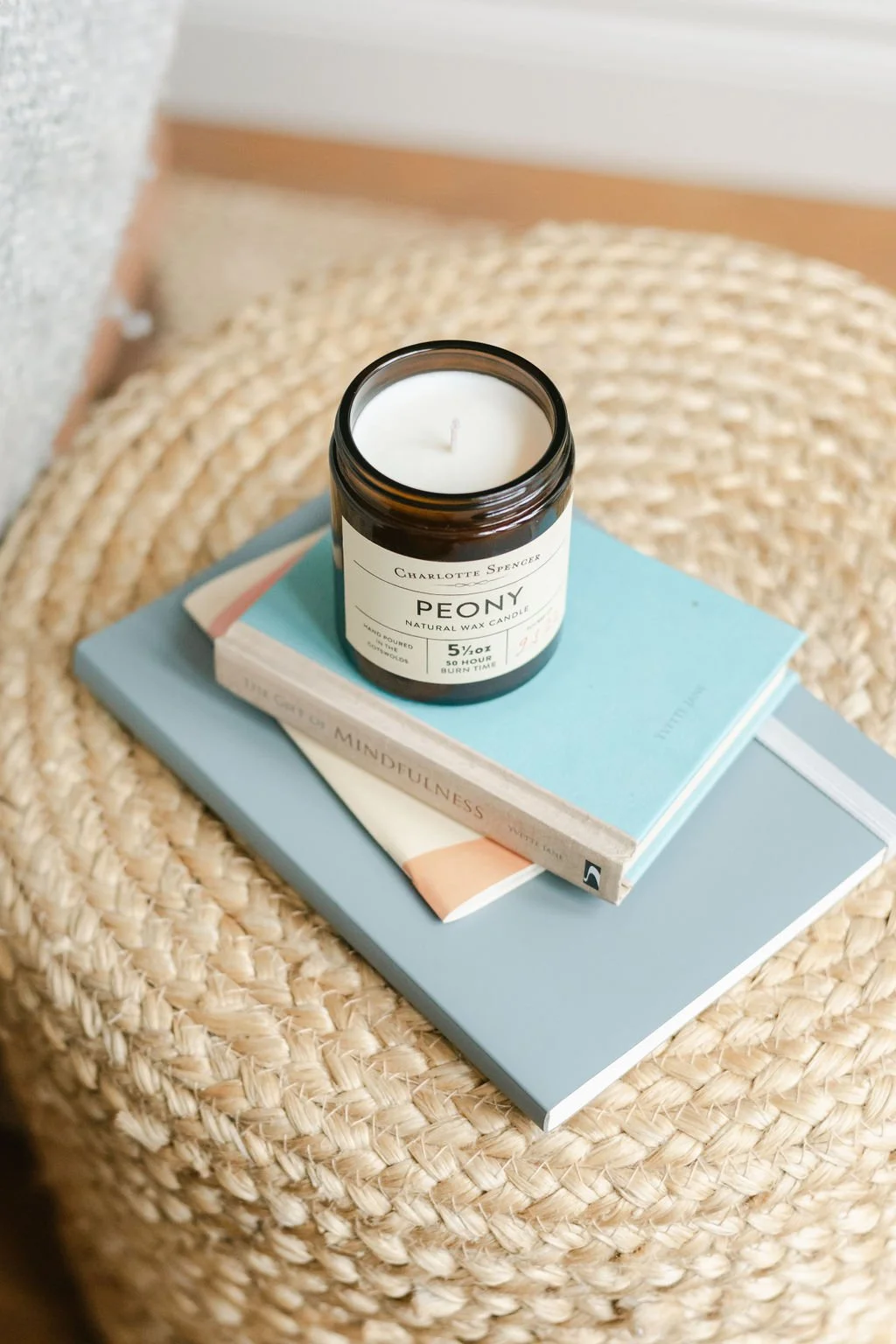 A candle resting on two stacked books, on a woven wicker surface.